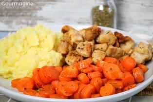 Steamed carrots, fried chicken pieces and mashed potatoes served on a white plate