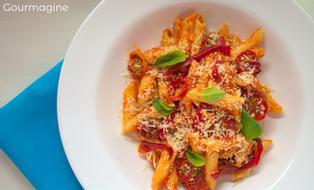 Penne mit getrockneten Cherrytomaten und Basilikumblättern angerichtet in einer weissen Schüssel