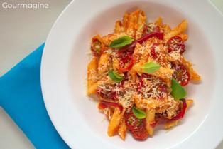 Penne with dried cherry tomatoes and basil leaves arranged in a white bowl