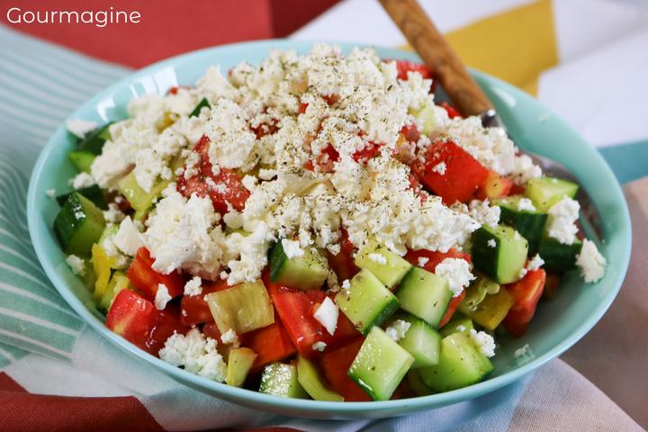 A green bowl filled with cucumbers, tomatoes, pepperoni and cheese