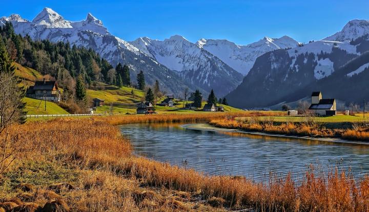 Bild einer grünen Naturlandschaft mit einem kleinen See und Schneebergen
