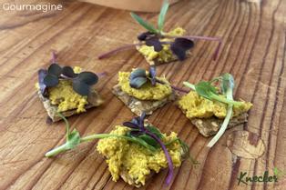 Five KNECKER crackers topped with Naturikum Fire Cider spread and Umami microgreens on a wooden table