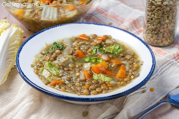A white soup plate filled with lentils, carrots and Chinese cabbage on a white fabric