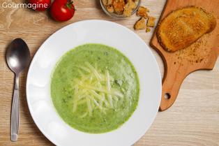 Green chard soup in a white plate on a wooden table with a freshly cut bread