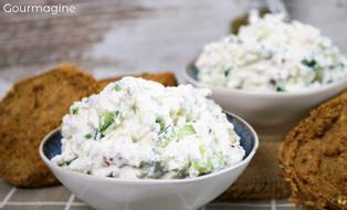 Zwei Schüsseln gefüllt mit Gurken-Käse-Salat neben mehreren dunklen Brötchen