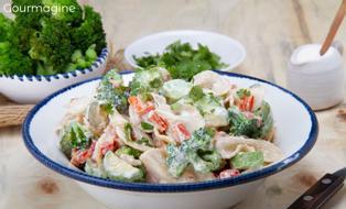 A white bowl filled with farfalle, broccoli, peppers and courgettes covered with a salad dressing